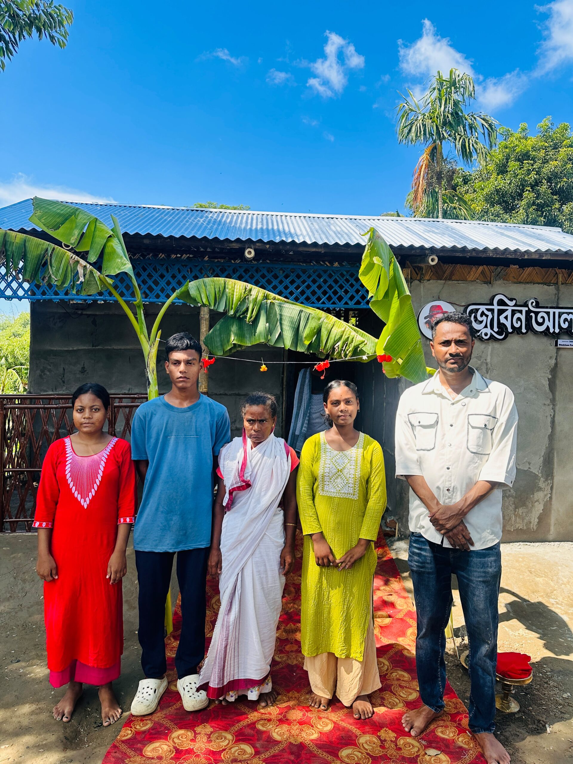 A flood-affected family standing in front of their new home, Zubeen Aloy, in Sivasagar